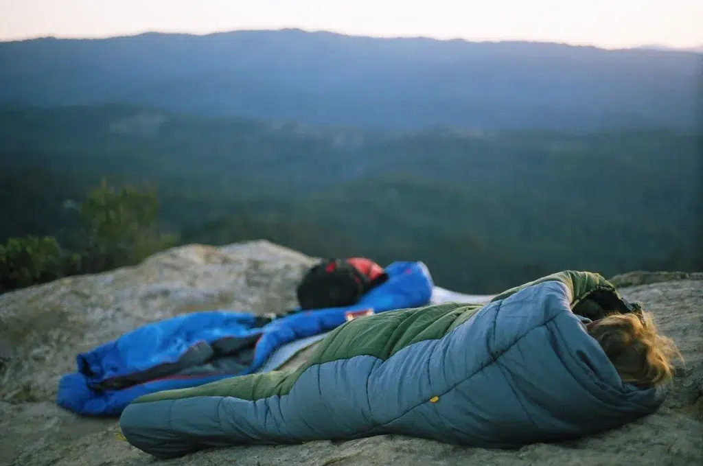 man sleeping on a mountain in a sleeping bag while camping